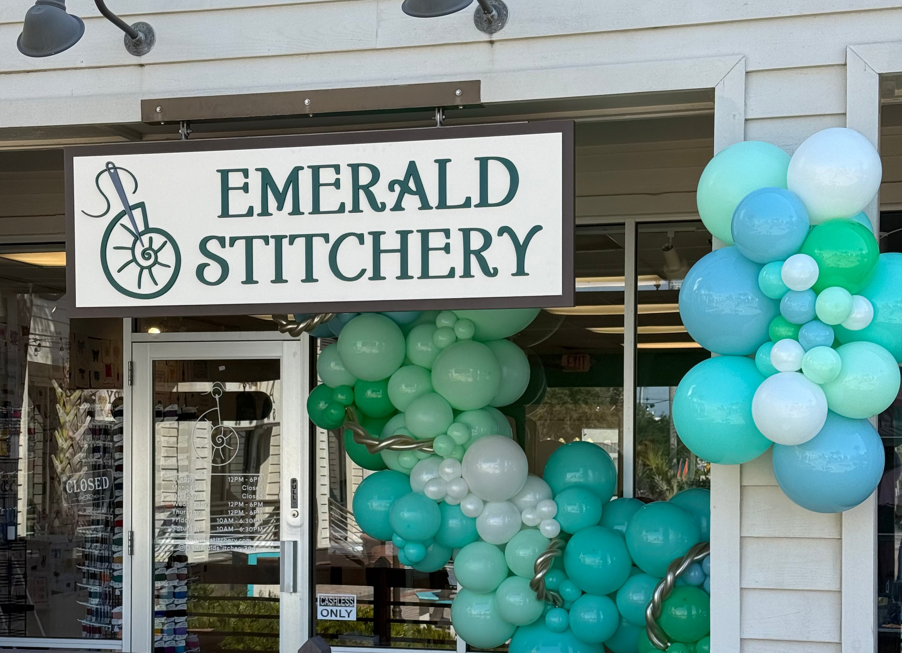 Storefront with 'Emerald Stitchery' sign and balloon decorations.